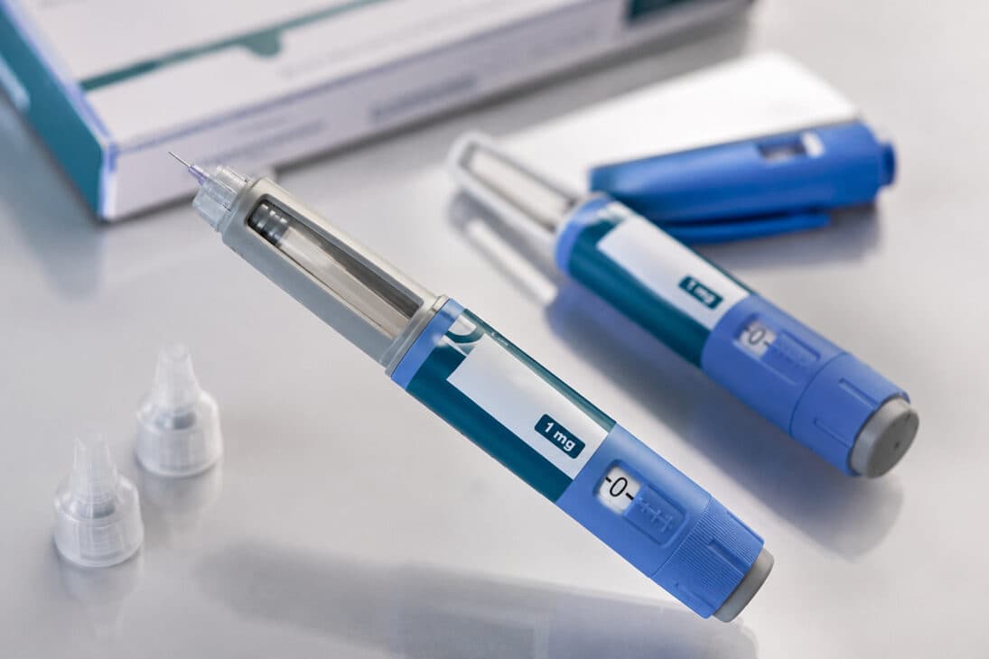 Caneta injetável de medicamento associado ao GLP-1 ao lado de embalagem farmacêutica sobre uma superfície.