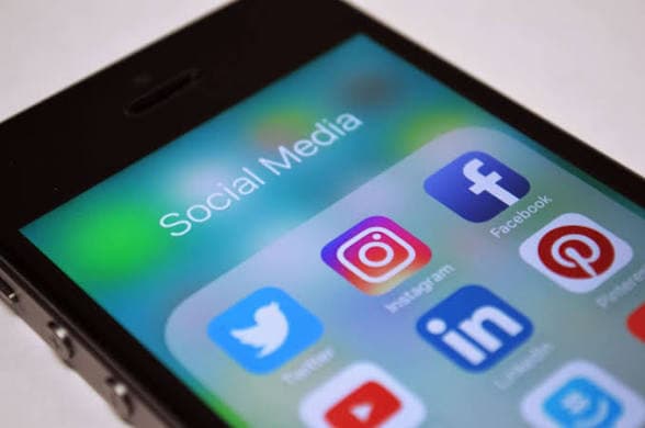 Celular exibindo redes sociais e anúncios digitais ao lado de uma urna eletrônica com elementos que representam as Eleições 2026